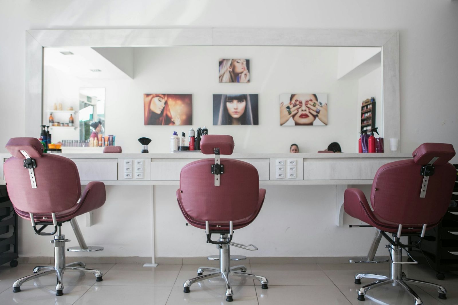 A bright salon styling station with three chairs facing a full-width mirror