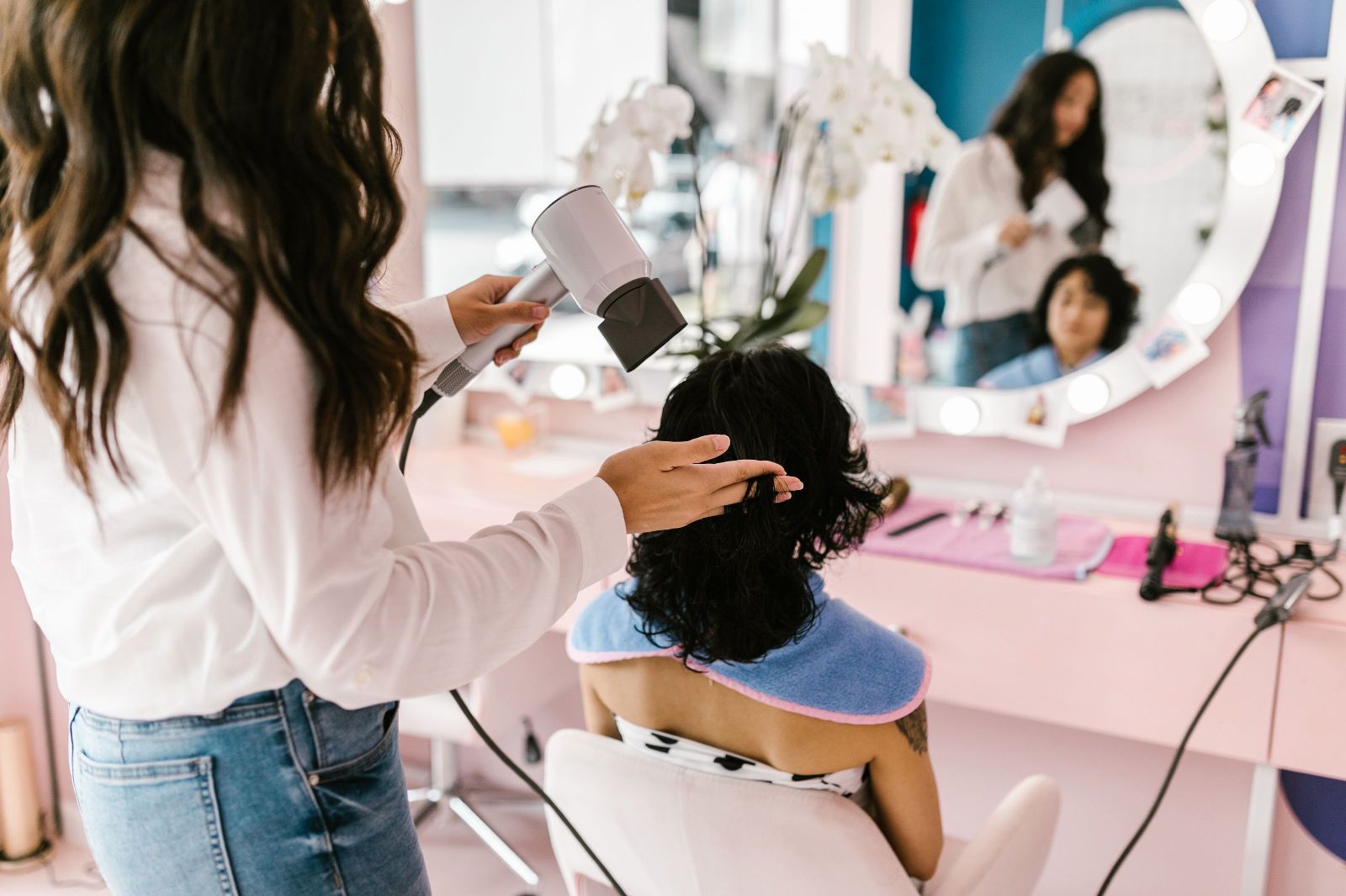 Stylist blow-drying a client’s hair at a salon station with a ring-lit mirror