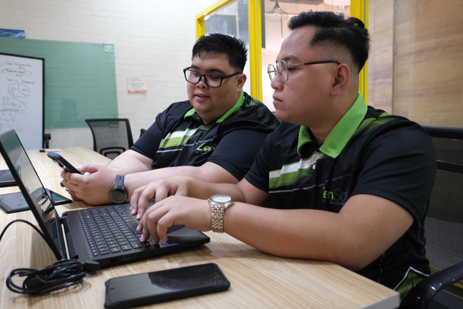 Two ZenSoft developers working through a build together at a laptop, a whiteboard behind them