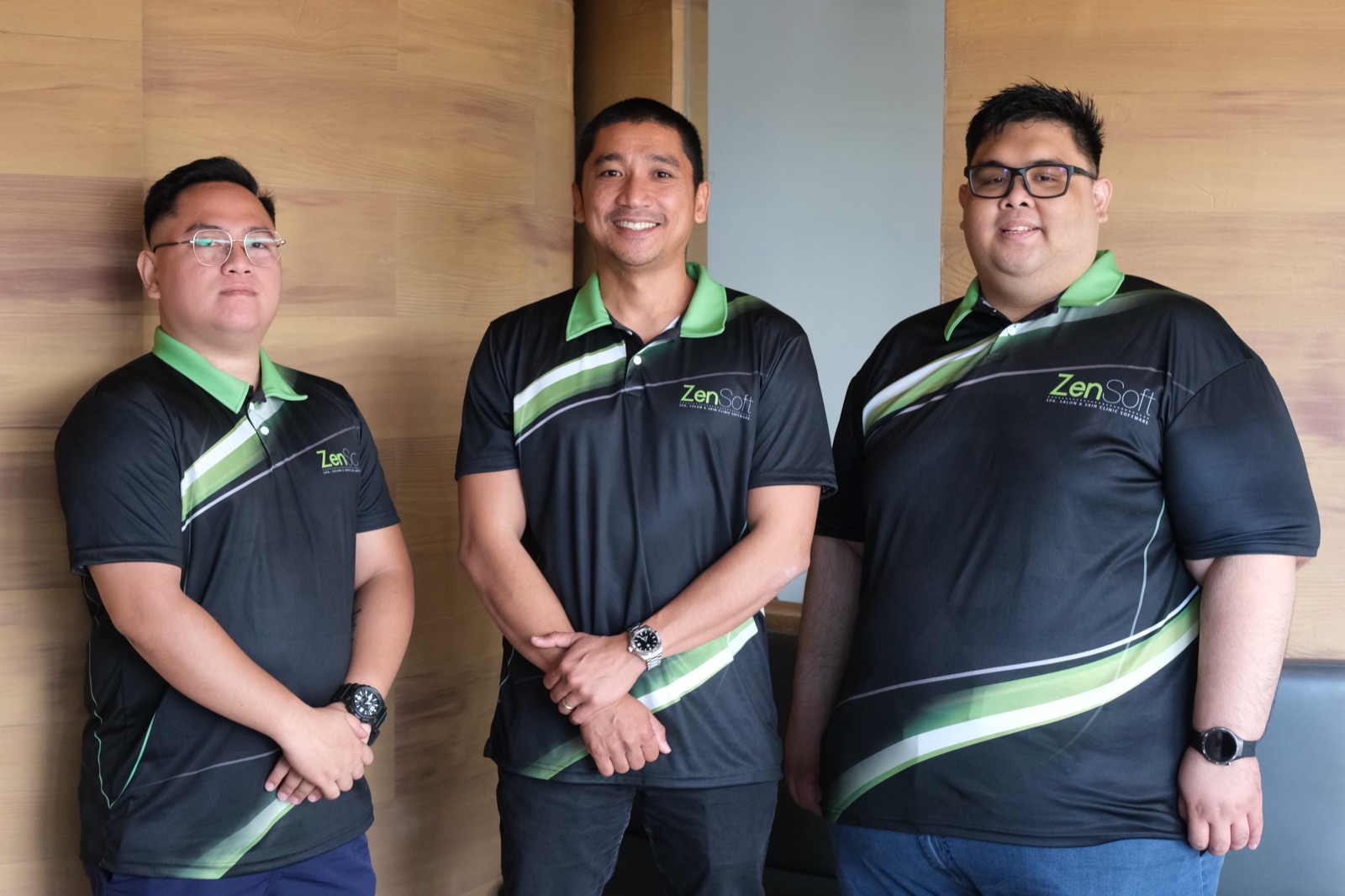 Three ZenSoft team members in branded polo shirts, standing against the office wood panel wall